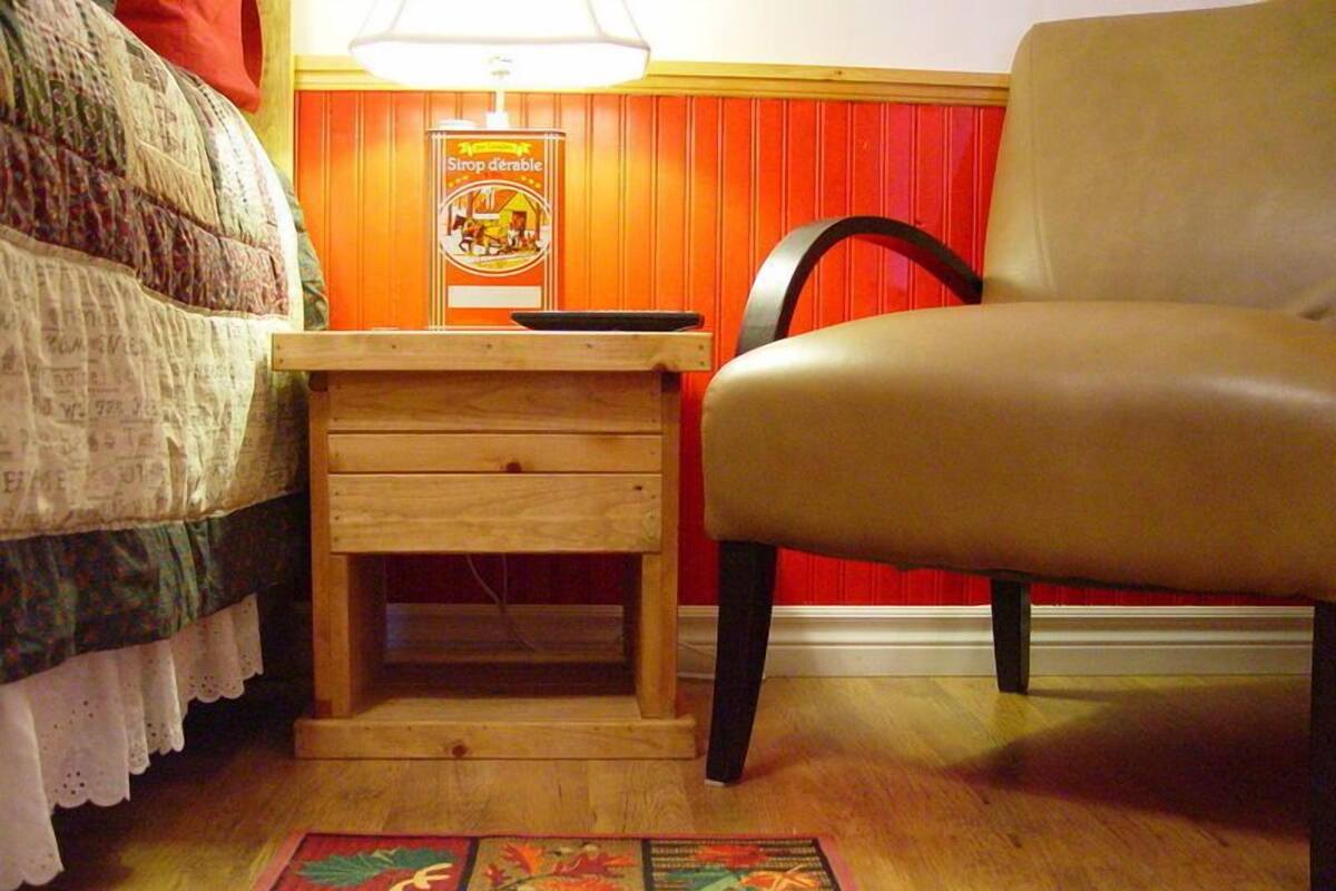 Una habitación con mesita de noche de madera, una silla, cama acolchada, pared roja y alfombra estampada.