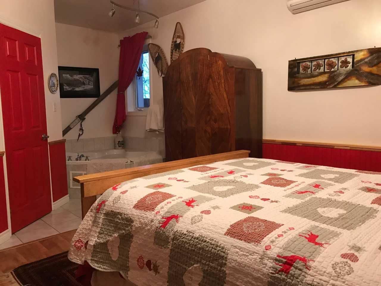 A bedroom with a bed, a wooden wardrobe, a red door, a staircase, and a wall-mounted picture.