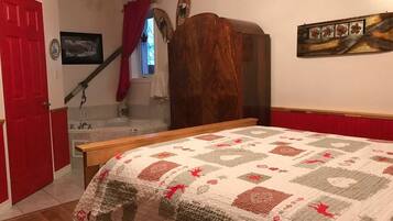 A bedroom with a bed, a wooden wardrobe, a red door, a staircase, and a wall-mounted picture.
