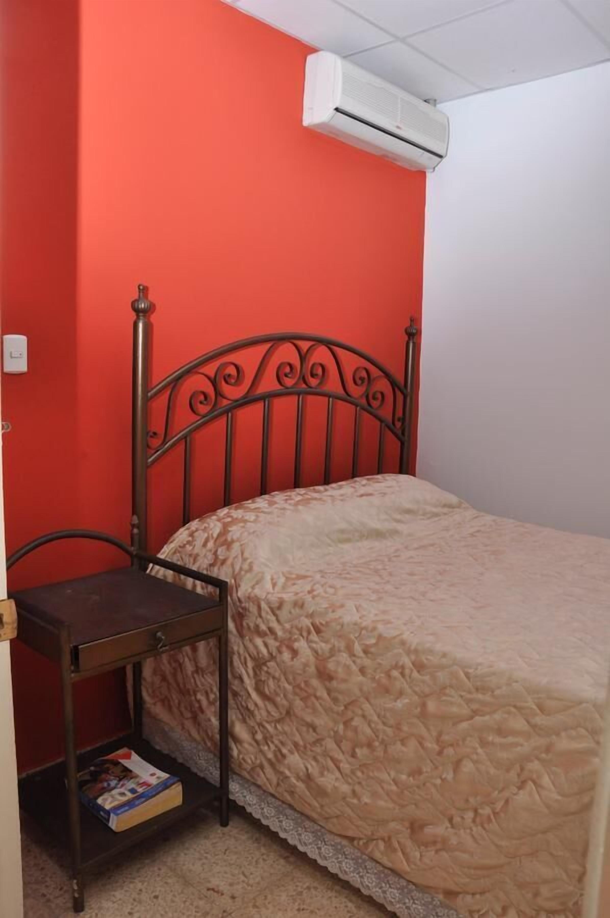 A room with a bed, a nightstand, and a red wall.