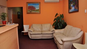 A reception area with a wooden desk, beige leather sofas, a potted plant, and two framed paintings on the walls. - Hotel Monumental (Santo Domingo)