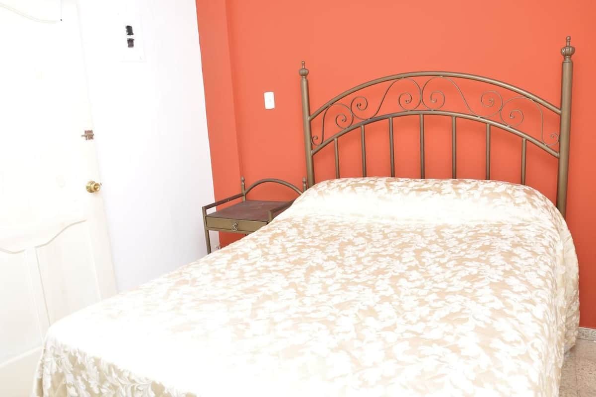 A single bed with a metal headboard in a room with a white door and an orange wall.