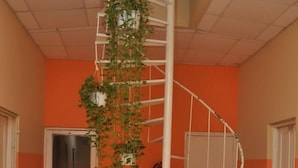 A spiral staircase with a white metal railing, surrounded by orange walls and a tiled floor. - Hotel Monumental (Santo Domingo)