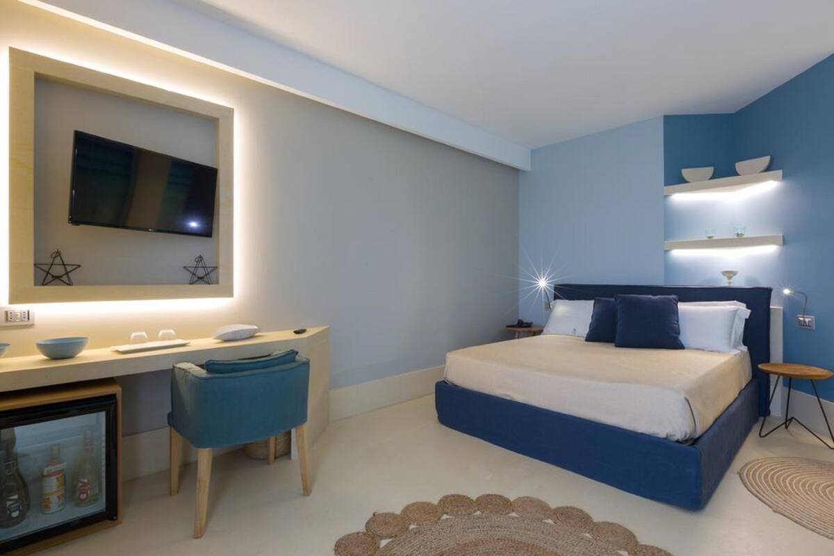 A modern bedroom with a large bed, a desk with a mirror, and a TV mounted on the wall.