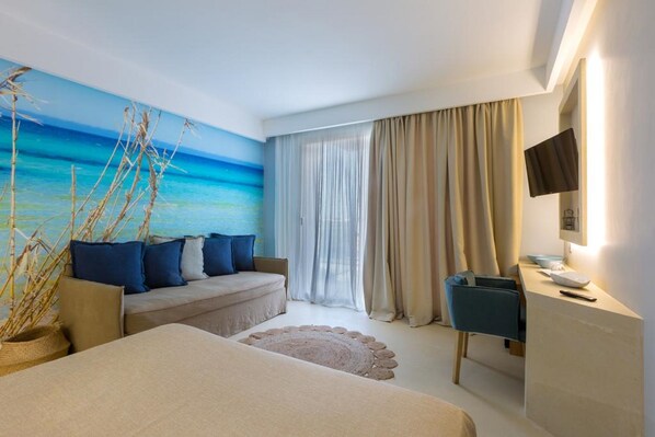 A modern hotel room with a large beach mural, a sofa with blue cushions, a desk area, and a bed. - Terra D'acqua Resort & Spa (Ugento)