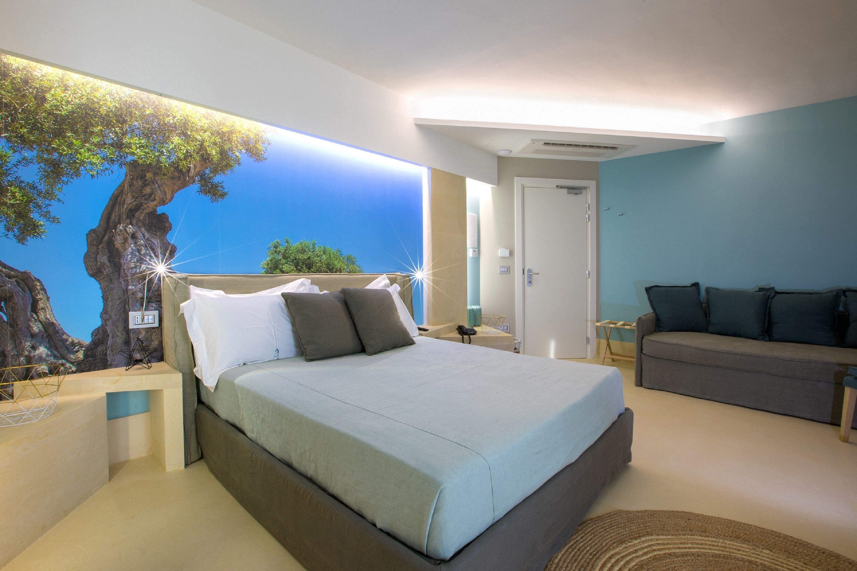 A bedroom with a bed, a sofa, a wall mural, and a nightstand.