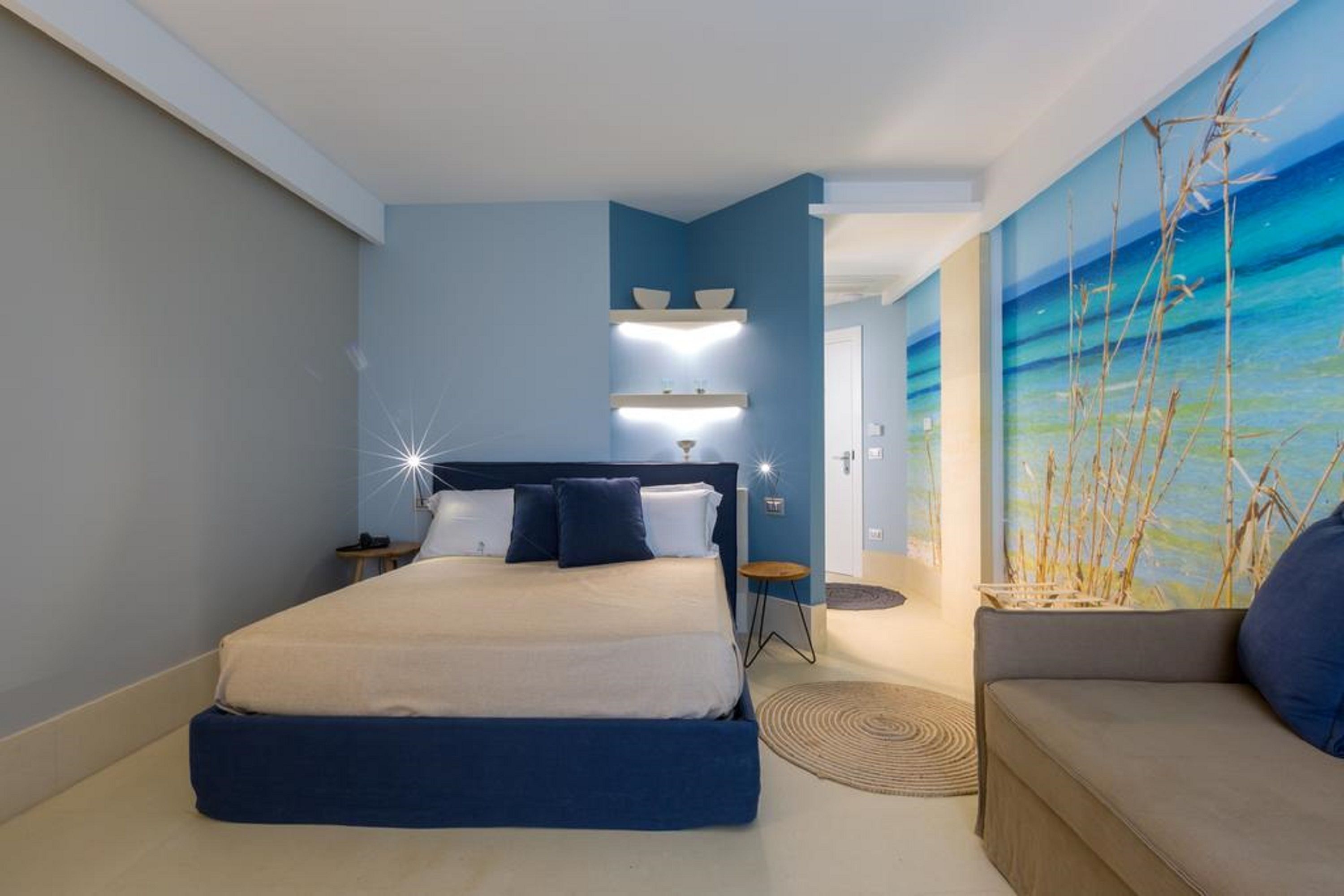 Une chambre moderne avec un grand lit, une table de chevet, une étagère fixée au mur et un tableau représentant une scène de plage.