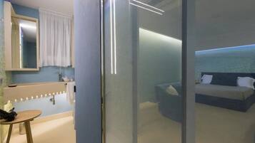 Una habitación de hotel moderna con un separador de vidrio, un baño con espejo y tocador, y una cama con vista al mar.