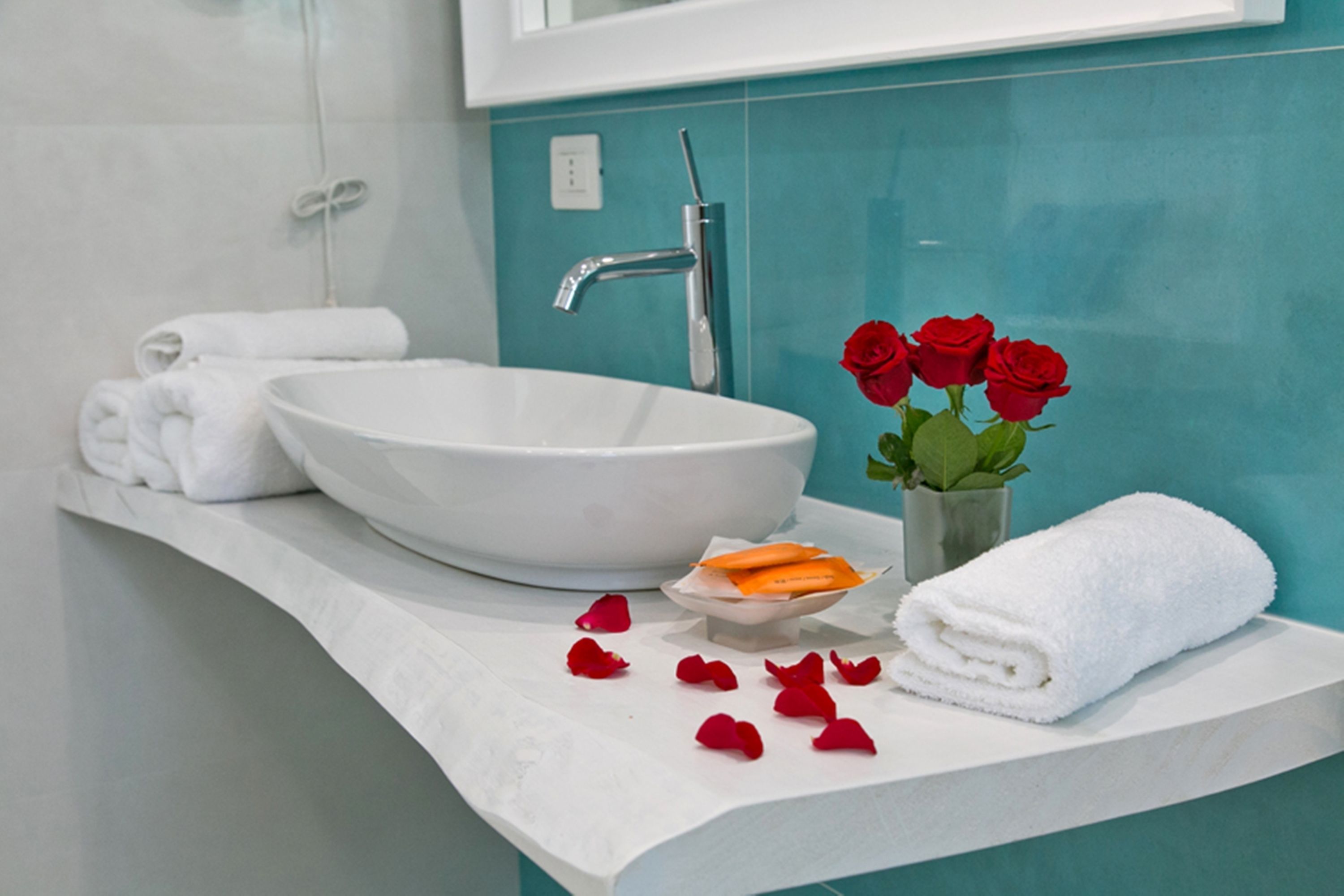A bathroom with a white sink, a mirror, and a teal wall. There are towels and red roses on the counter.