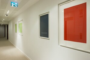 A hallway with framed artworks on the walls, a door, and a ceiling sign indicating an exit.