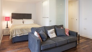 Um quarto moderno com uma cama, um sofá cinza e uma mesa de cabeceira com uma luminária.