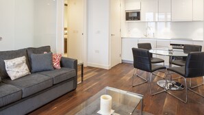 Uma sala de estar moderna com um sofá cinzento, cadeiras pretas e uma mesa de centro de vidro.