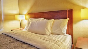 Una habitación de hotel con una cama, dos lámparas de noche y un cabecero de madera.