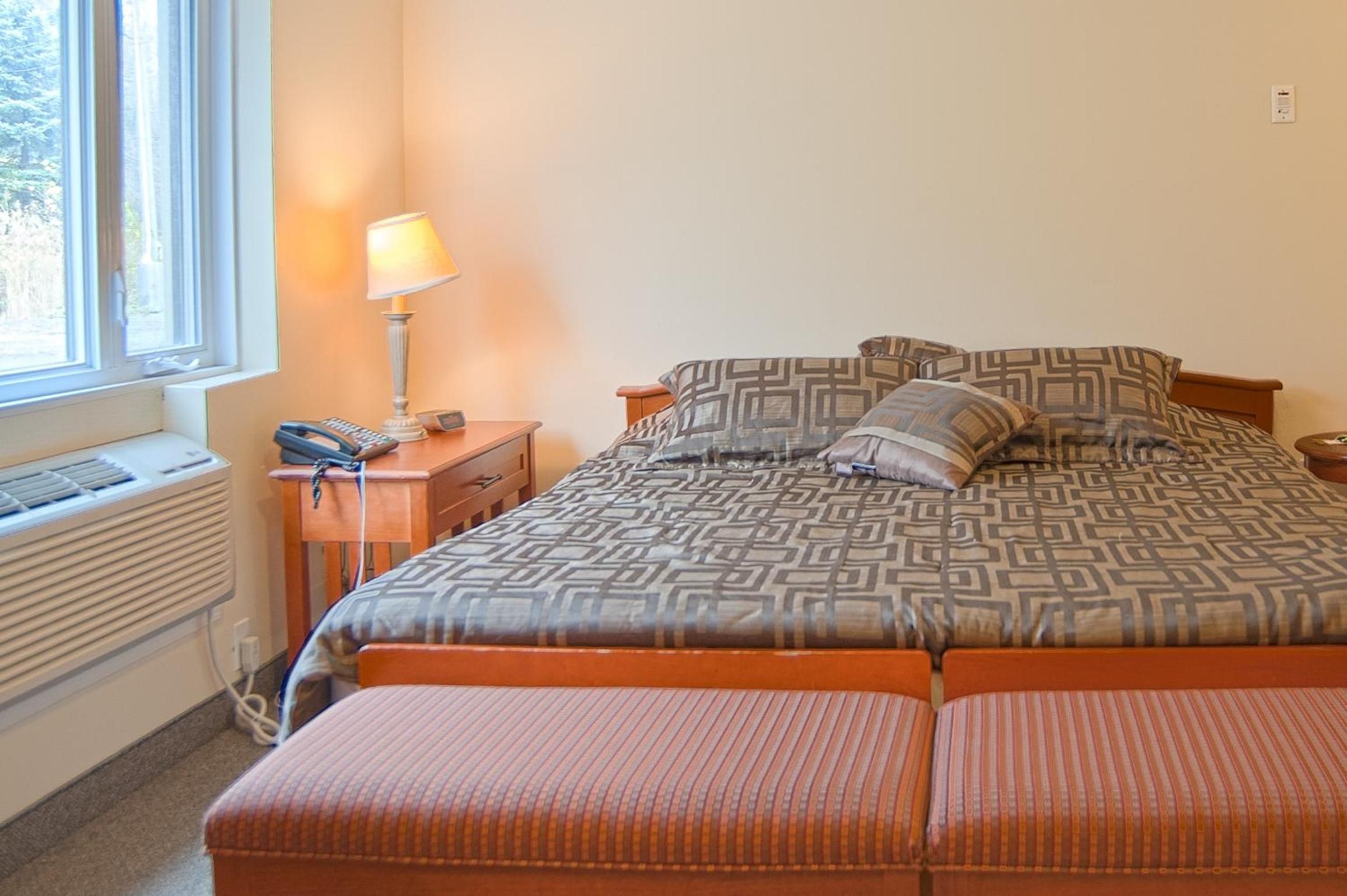 Un dormitorio con una cama, mesitas de noche, una lámpara y una ventana.