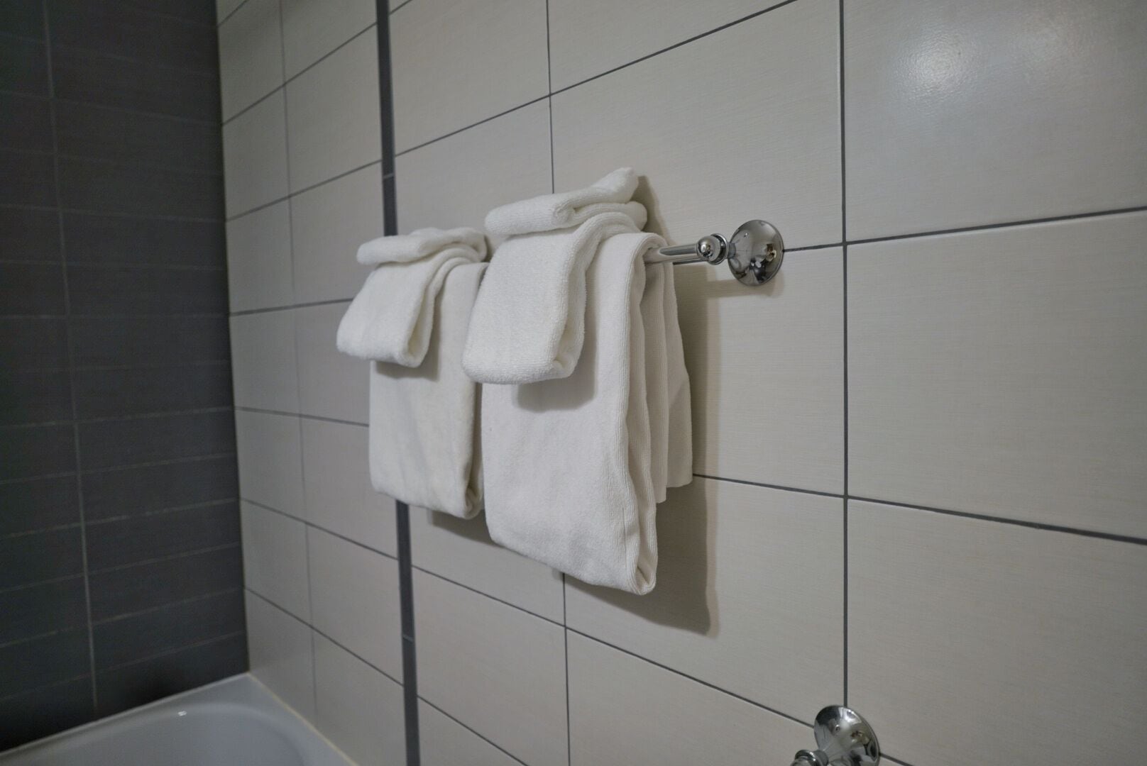 A bathroom with white tiled walls, a white bathtub, and a towel rack with two towels.