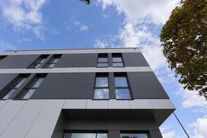 A modern building with a flat roof, rectangular windows, and a visible tree branch.