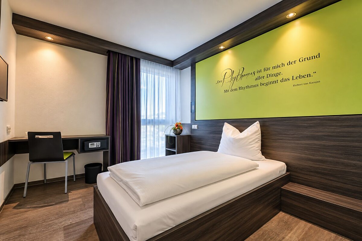Habitación de hotel con cama, escritorio, silla, cesto de basura y una pared con una cita.