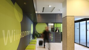 Un área de recepción con decoración en tonos verde y negro, una mesa de recepción y una planta en maceta.