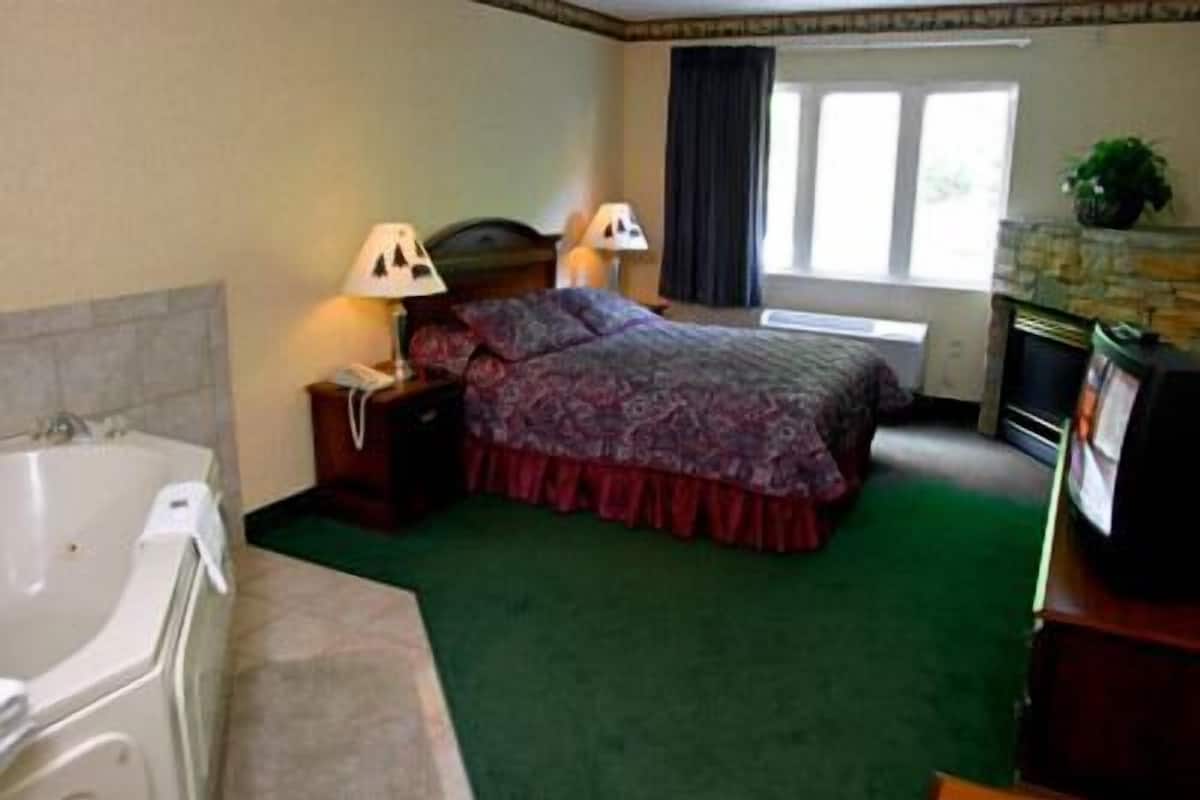 A hotel room with a large bed, two bedside lamps, a fireplace, a bathtub, and a window with curtains.