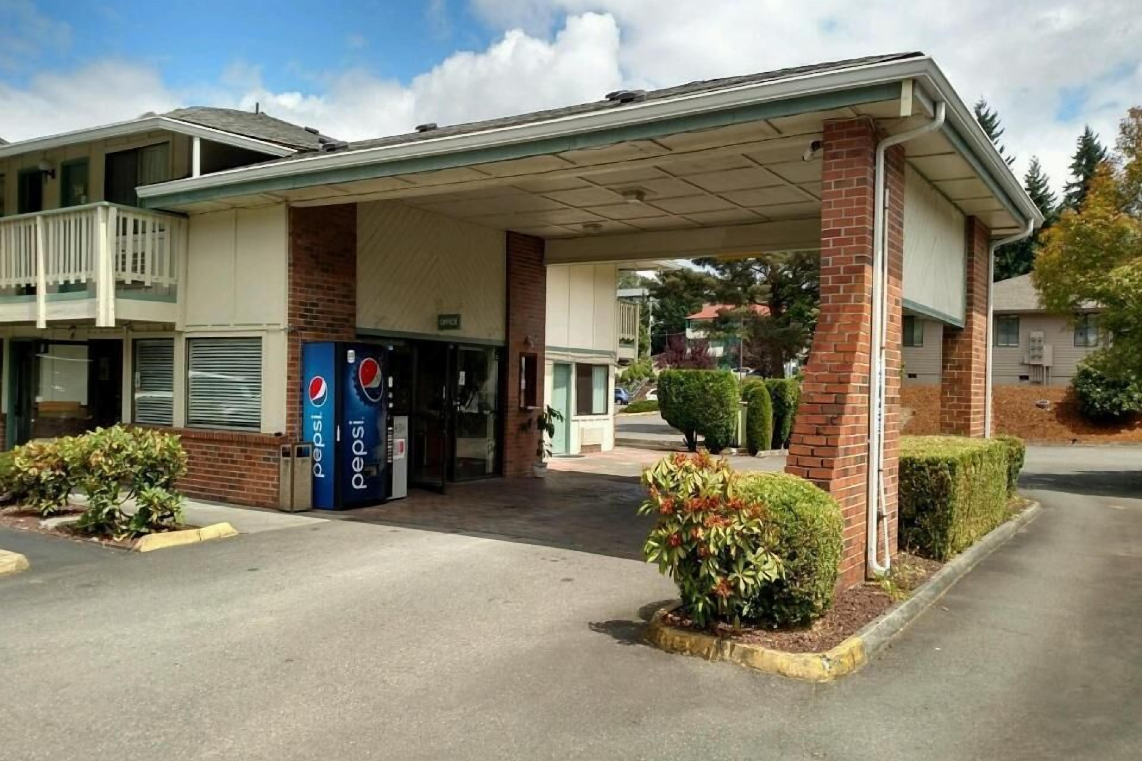 A motel with a covered parking area, a Pepsi vending machine, and a small garden with bushes.