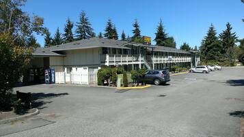 Un motel con un área de estacionamiento cercada, una máquina expendedora de Pepsi y un letrero que anuncia el motel y un servicio de remolque.