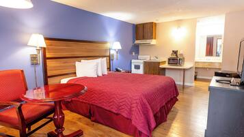 Una habitación de hotel con una cama, un escritorio, un microondas, una estufa y una silla.