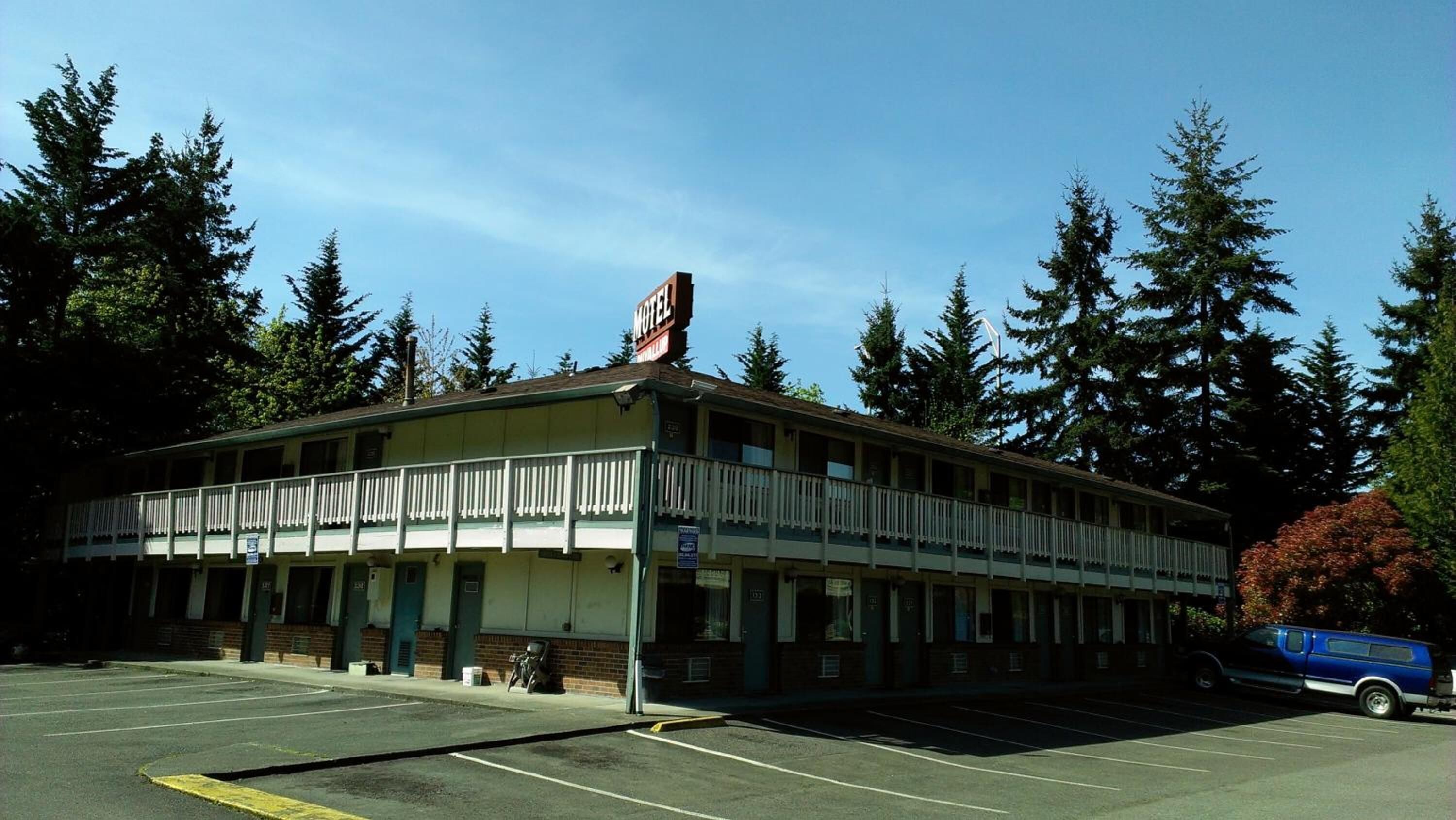 A motel with a two-story structure, a balcony on the second floor, and a parking lot in front.