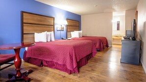 Habitación de hotel con dos camas, una mesa de madera, un escritorio con una computadora y un televisor.