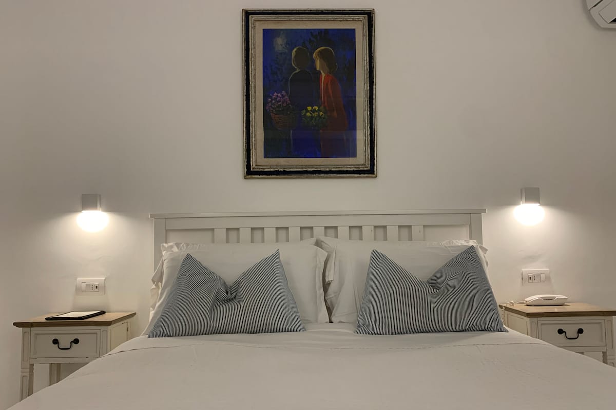 A neatly made bed with striped pillows, a framed painting above, and bedside lamps on nightstands.