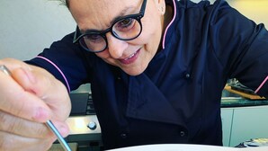 Una persona con delantal de chef negro sosteniendo una cuchara sobre un postre en un plato blanco.