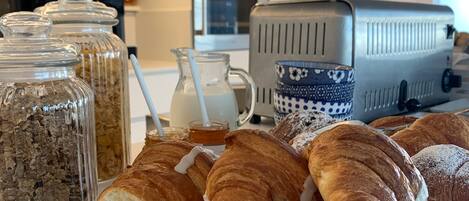 Um buffet de café da manhã com pães, uma máquina de café e potes de acompanhamentos.