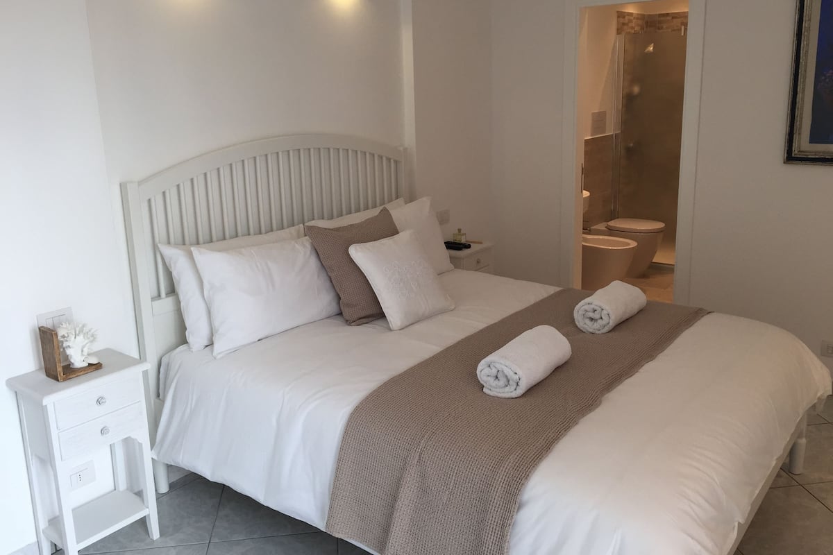 A bedroom with a bed, nightstand, and a bathroom visible through an open door.