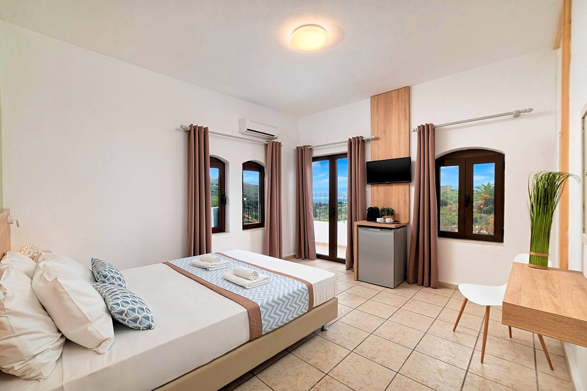 A hotel room with a bed, a desk, a TV, and a view of the outdoors.