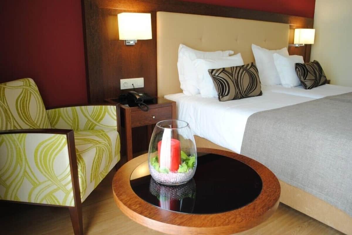 A hotel room with a bed, a chair, a bedside table with a lamp, and a decorative glass vase.