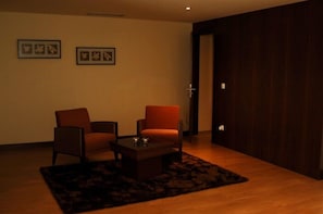 Una habitación con dos sillas, una mesita y un tapete oscuro sobre piso de madera.