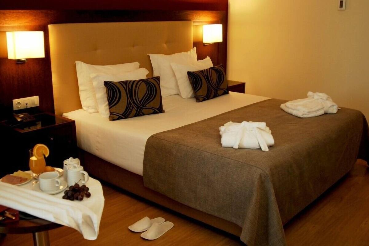 A hotel room with a large bed, two bedside tables, a nightstand, and a table with breakfast items.