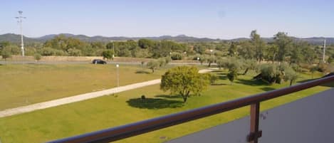 A balcony with a view of a grassy area, trees, and distant hills.