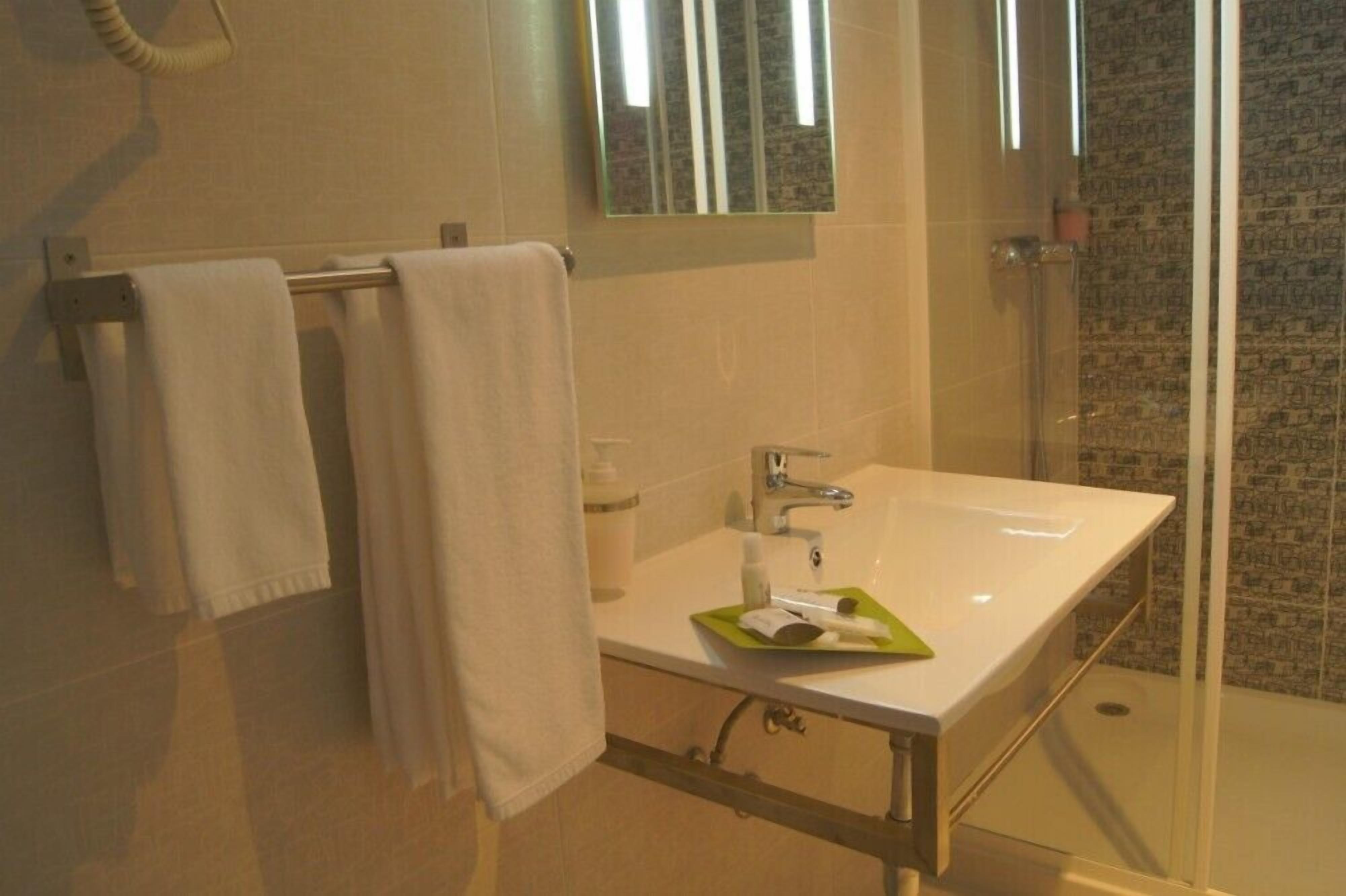 A bathroom with a white sink, a glass shower enclosure, and a towel rack with two white towels.
