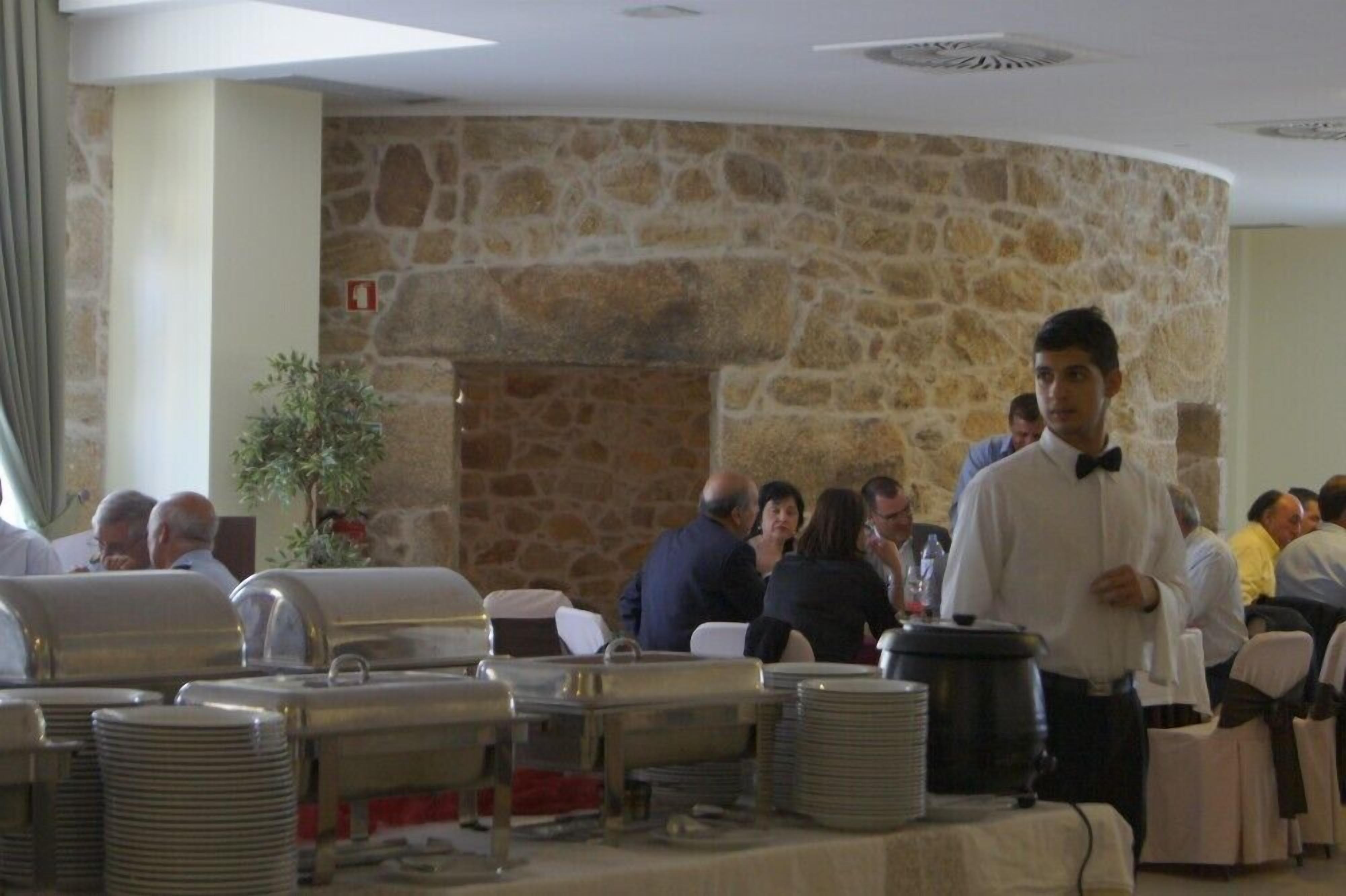 A buffet setup with stacked plates and a buffet station in a room with stone walls and a ceiling vent.