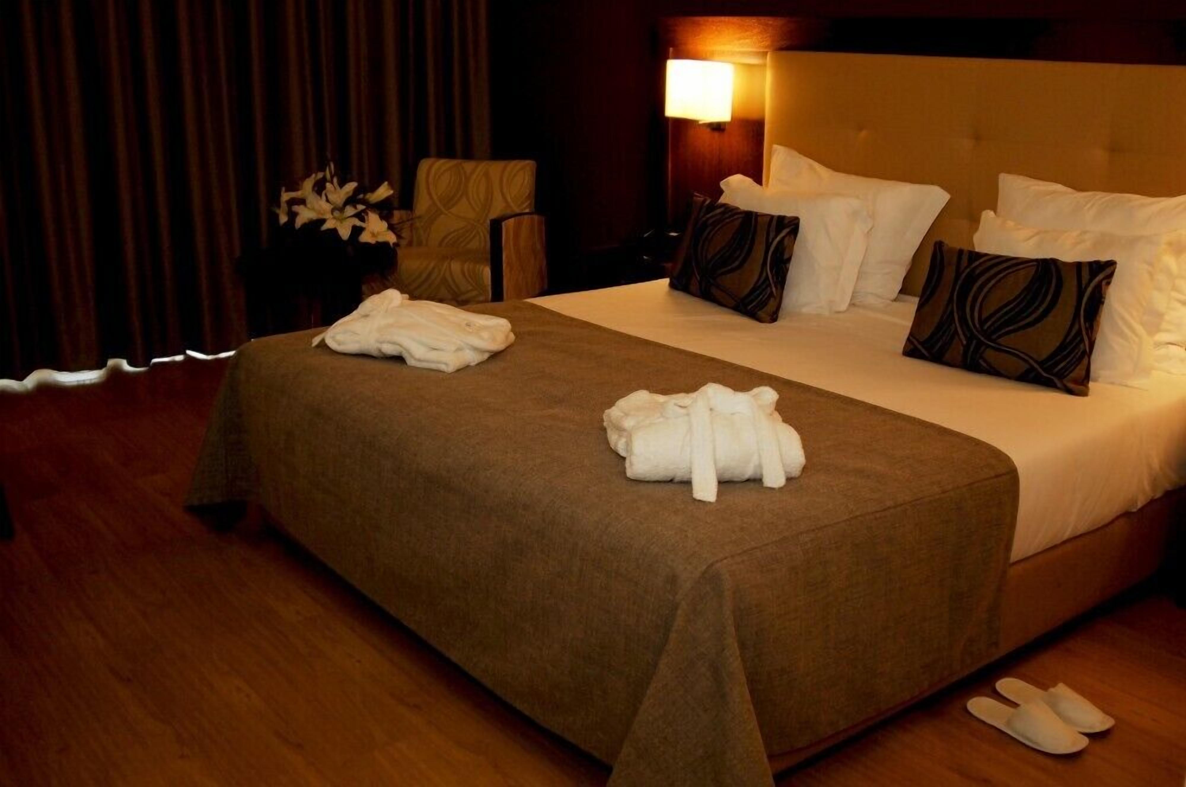 A hotel room with a large bed, a chair, a lamp, and a vase with flowers.
