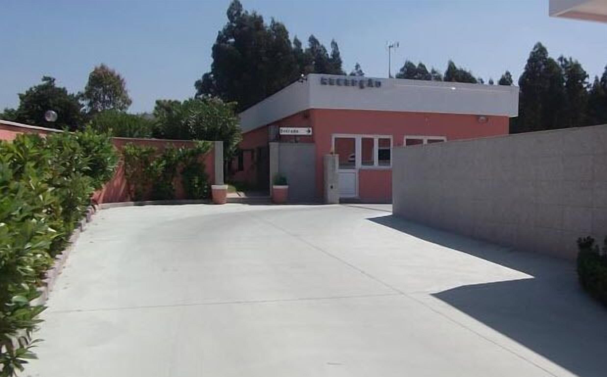 Un edificio con fachada roja y blanca, techo plano y zona de entrada pavimentada.