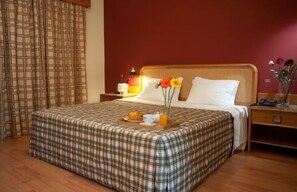 Una habitación de hotel con una colcha escocesa, una mesita de noche con lámpara y una bandeja con productos para el desayuno.