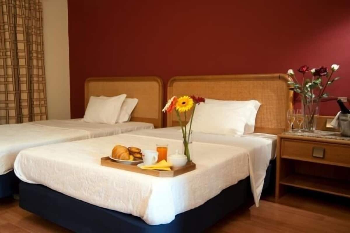 Ein Hotelzimmer mit zwei Betten, einem Frühstückswagen und einer Vase mit Blumen.