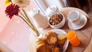 Bandeja de desayuno con cruasanes, mermelada y jugo de naranja, junto a un florero con flores y un tazón de granola.