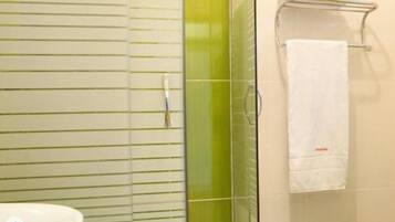 A bathroom with a glass shower enclosure, a white sink, and a towel rack with a white towel.