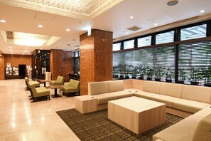 A modern lobby with a large sectional sofa, green chairs, and a coffee table. - Marroad Inn Omiya (Saitama)