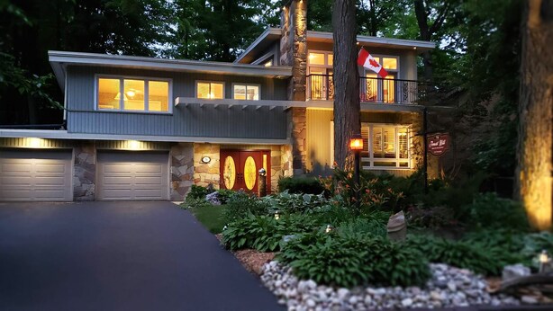 A two-story house with a stone facade, a flag, and a driveway leading to a garage. - Forest Hill Bed & Breakfast (Kitchener)