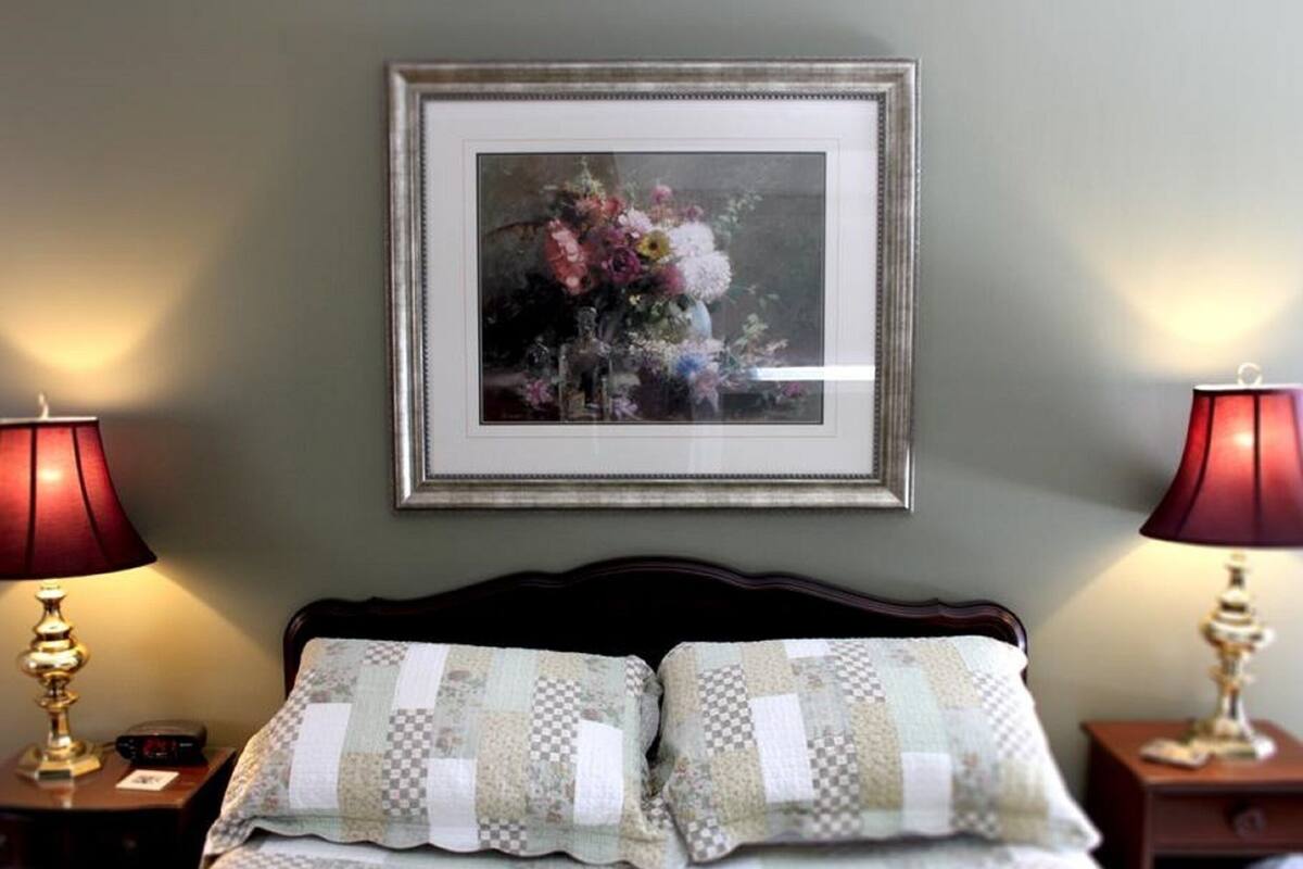 A neatly made bed with two pillows, a framed floral artwork above it, and two bedside lamps on either side.