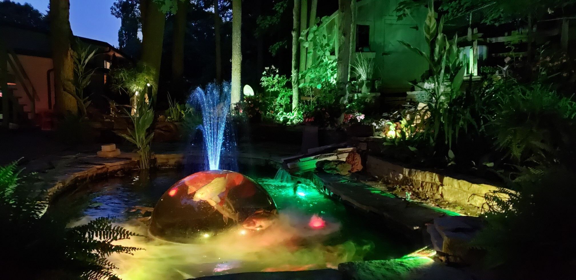 Ein Garten mit einem Wasserspiel, darunter ein Brunnen und ein Teich mit einem großen Stein.