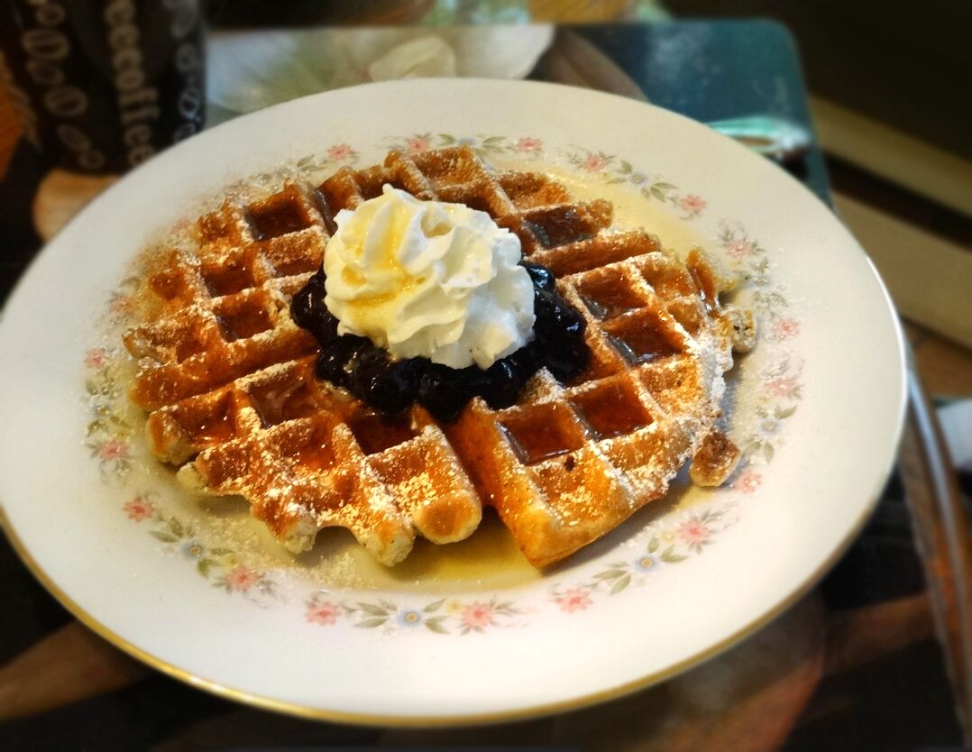 A plate with a waffle, whipped cream, and a berry compote.